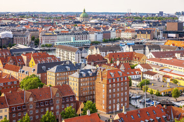 Panoramic view of Copenhagen taken from the top of the Church of Our Saviour, showing a mix of historical rooftops, modern buildings, and city landmarks under a warm evening sky.