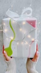 Woman's Hands Holding a Gift Wrapped in Pink and Green Abstract Design with Silver Lights