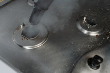 Close-up steam cleaning gas stove surface, eliminating burned food and grease, restoring kitchen...