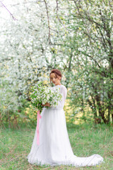 A young girl in a white dress holds a bouquet of flowers, standing against the background of...