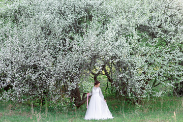 A young girl in a white dress among flowering trees, surrounded by spring greenery, creates an...