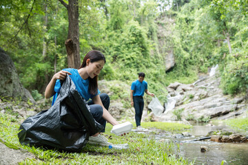 Fototapeta premium Volunteer Team Cleaning Riverbank. A dedicated volunteer collects plastic waste from a riverbank while another assists.