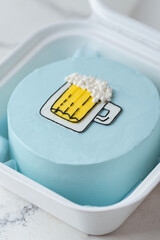 Small bento cake with blue cream cheese frosting decorated with a glass of foaming beer drawing in a gift box. Trendy cake as a gift for a beloved man