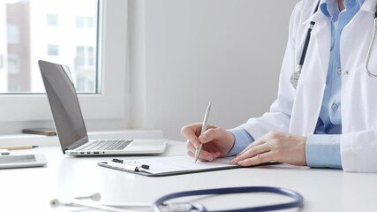 Female doctor completing healthcare paperwork, clipboard positioned near laptop and stethoscope in well lit clinical workspace by window. Medicine and health care concept - Powered by Adobe