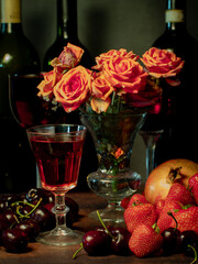 Still life with rose flowers, summer fruits, bottles of wine and a glass of wine. Pomegranate, cherry, sweet cherry, strawberry and watermelon. Alcohol. The still life is stylized as an old painting.