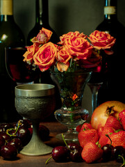 Still life with rose flowers, summer fruits, bottles of wine and a glass of wine. Pomegranate, cherry, sweet cherry, strawberry and watermelon. Alcohol. The still life is stylized as an old painting.