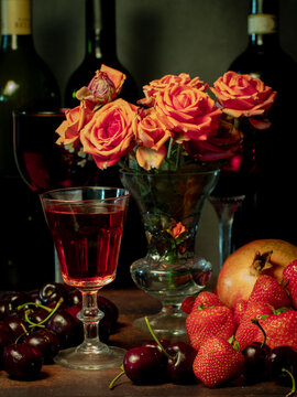 Still life with rose flowers, summer fruits, bottles of wine and a glass of wine. Pomegranate, cherry, sweet cherry, strawberry and watermelon. Alcohol. The still life is stylized as an old painting.