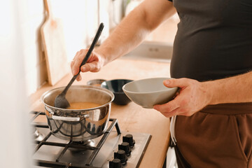 Man cooking ramen noodles. Male making noodle soup broth in the home kitchen stove. Traditional Asian food. Close Up Photo Of Mans Hands Serving Pasta With Fresh Vegetables. Preparing Homemade Dish.