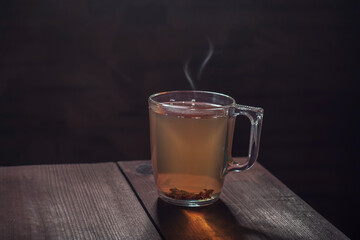 Black hot tea  with wavy steam stands on the edge of the table.