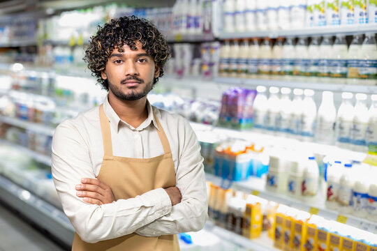 A supermarket employee stands confidently with arms crossed, in front of a dairy aisle, presenting a professional, friendly demeanor. - Powered by Adobe