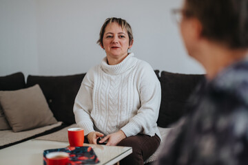 An elderly woman sits in her cozy living room, engaging in a warm conversation with a guest. She...