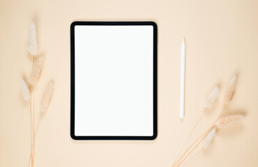 Blank tablet on a beige surface with a pen and decorative dried plants arranged artistically