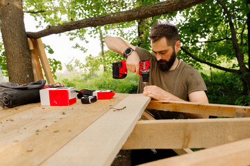 young brunette man, dad with beard is nailing building a tree house to his little son with wooden...