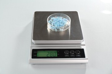 Scale with Petri dish of sample on white mirror table, closeup
