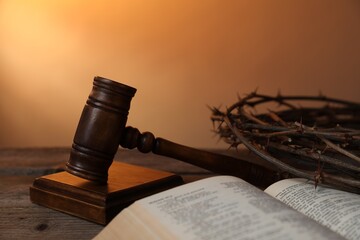 Judge's gavel, crown of thorns and Bible on wooden table against pale orange gradient background,...