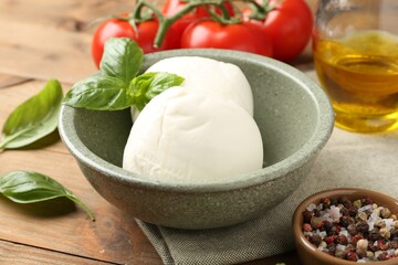 Tasty mozzarella balls, tomatoes, oil and basil on wooden table, closeup