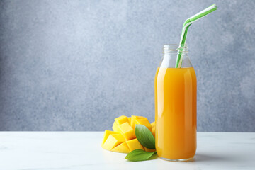 Tasty mango juice in glass bottle, fresh fruit and green leaves on white marble table, space for text