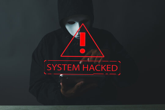 Technology idea.,An anonymous hacker in a mask and hoodie with a 'System Hacked' warning message. Concept for a cyber attack, data breach, cybersecurity threat,computer virus,data privacy,hacker.