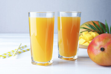 Tasty mango juice in glasses, fresh fruits, straws and green leaves on white wooden table, closeup