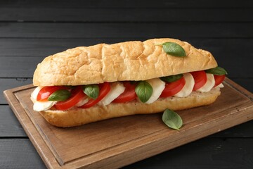 Tasty sandwich with mozzarella cheese, tomatoes and basil on black wooden table, closeup