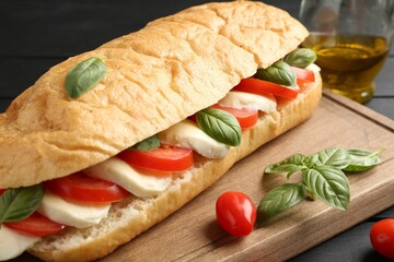 Tasty sandwich with mozzarella cheese, tomatoes and basil on black wooden table, closeup