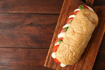 Tasty sandwich with mozzarella cheese, tomatoes and basil on wooden table, top view. Space for text
