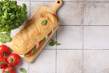 Tasty sandwich with mozzarella cheese, tomatoes and basil on light tiled table, flat lay. Space for...