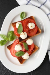 Tasty sandwiches with mozzarella cheese, tomatoes and basil on dark textured table, top view