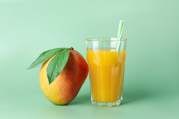 Tasty mango juice in glass and fresh fruit on green background