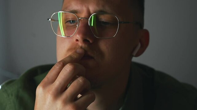 A person thinks about something and regrets.
A sad man in no mood sits in a dark room wearing headphones and glasses.
A man with poor eyesight is worried and thinking about something