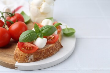 Tasty sandwich with mozzarella cheese, tomatoes and basil on light tiled table, closeup. Space for text