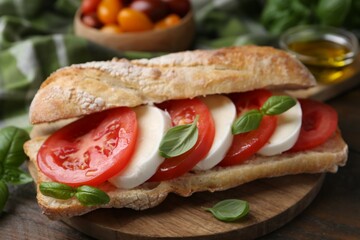 Tasty sandwich with mozzarella cheese, tomatoes and basil on wooden table, closeup