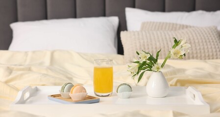Tray with delicious breakfast and flowers on bed indoors, closeup. Space for text
