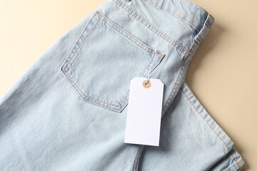 Light blue jeans with tag on beige background, top view