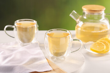 Tasty green tea in glass cups, teapot and lemon on white table outdoors, closeup