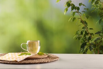 Tasty green tea in glass cup and leaves on white marble table outdoors, space for text