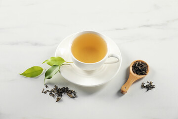 Tasty green tea in cup, brew and leaves on white marble table, above view