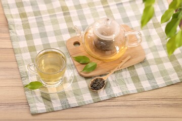 Tasty green tea in glass cup, teapot, brew and leaves on wooden table, above view