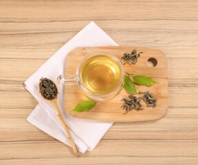 Tasty green tea in glass cup, brew and leaves on wooden table, flat lay
