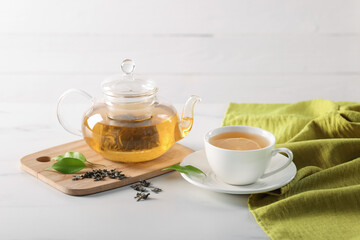 Tasty green tea with lemon in cup, teapot, brew and leaves on white marble table