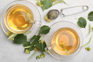 Fresh linden tea in cups and flowers on light grey table, flat lay