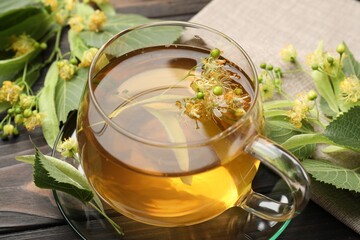 Fresh linden tea in cup and flowers on dark wooden table, closeup