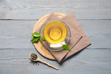 Tasty green tea with lemon in glass cup, brew and leaves on grey wooden table, flat lay