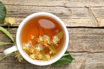 Tasty linden tea in cup, leaves and flowers on wooden table, flat lay