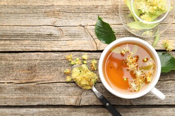 Tasty linden tea in cup, leaves and flowers on wooden table, flat lay. Space for text