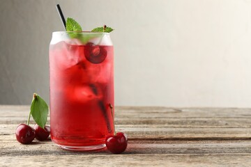 Tasty cherry soda with ice cubes, berries and mint on wooden table, closeup. Space for text