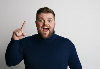 Excited Man in Blue Turtleneck Pointing Up – Portrait with Happy Expression, White Background, Ample Space for Text, High-Resolution Studio Photography for Advertising & Social Media Concepts