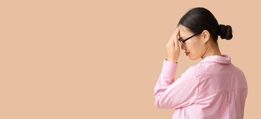 Young Asian woman suffering from headache on beige background with space for text