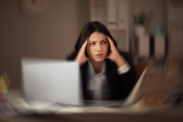 Tired young businesswoman with headache in office late in evening
