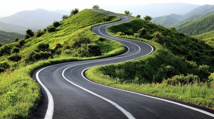 A winding road curves through lush green hills under a hazy sky with distant mountain ranges in the background.